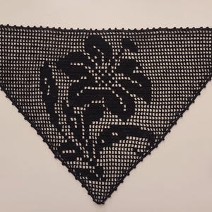 Puede incluir: Un pañuelo triangular de ganchillo negro con un intrincado patrón de rejilla calada y un motivo floral central. El accesorio está rematado con un delicado borde festoneado en la parte superior e incluye dos finas cintas en las esquinas.