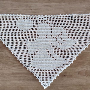 May include: A white triangular crochet bandana featuring a filet crochet pattern of a central angel figure holding a heart. The accessory has a delicate grid-like mesh construction with a scalloped edge and thin ties on each side with small floral accents.
