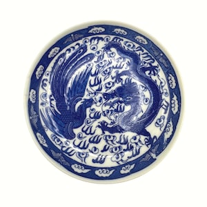 May include: Round, white ceramic plate with a blue dragon and phoenix design. The plate features a detailed illustration of the mythical creatures, surrounded by cloud and wave patterns. The rim has a blue border with a repeating cloud motif.