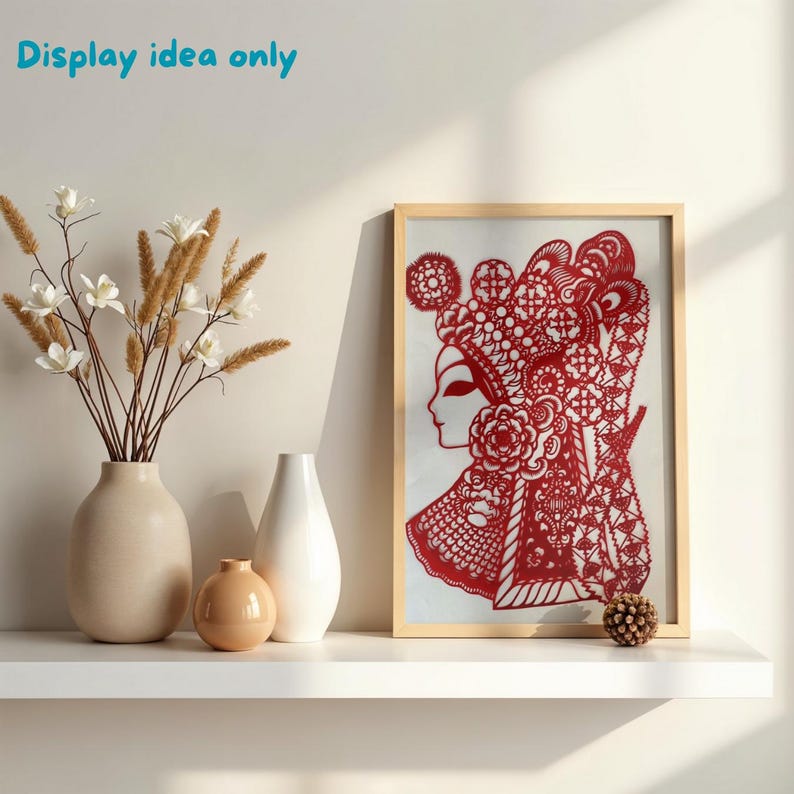 May include: A framed red paper cut-out of a woman in traditional Chinese opera attire. The artwork is displayed on a white shelf with vases and decorative flowers. The text "Display idea only" is in the upper left corner.