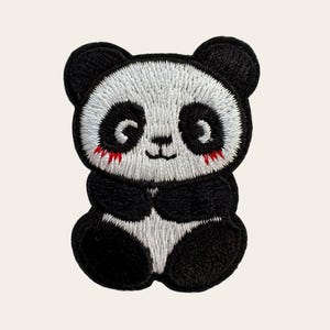 May include: An embroidered patch featuring a stylized panda bear with a white face, black ears, and black eye patches. The panda has small red stitched accents under its eyes, a black nose, and a simple black mouth line, with a black and white body.