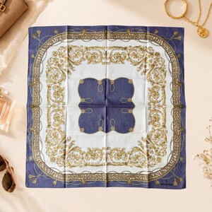 May include: A square scarf featuring a deep blue and white color palette with an ornate gold-toned filigree border. The center displays a dark blue four-lobed shape outlined in gold, surrounded by intricate scrolling patterns and chain motifs.