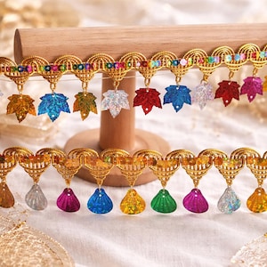 May include: Decorative gold trim with colorful leaf and teardrop pendants. The trim features a repeating pattern of gold filigree with iridescent and jewel-toned accents. The pendants include maple leaf and teardrop shapes in various colors.