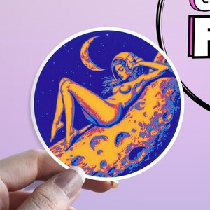 May include: Round sticker featuring a retro illustration of a woman in a space helmet reclining on a moon. The artwork uses shades of yellow, blue, and orange against a dark blue starry background.