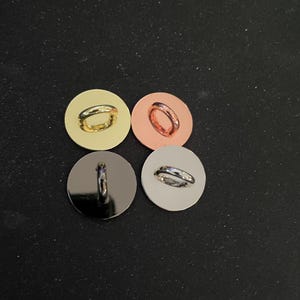 May include: Four metal buttons in gold, copper, black, and silver. Each button has a small loop for attaching to fabric. The buttons are round and have a shiny finish, suitable for various sewing projects.
