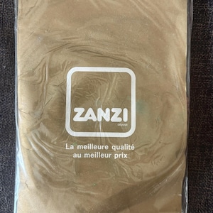 Può includere: Una confezione rettangolare color oro avvolta in plastica trasparente. Al centro presenta un logo quadrato bianco con angoli arrotondati contenente il testo ZANZI e la parola déposé. Sotto il logo c'è il testo La meilleure qualité au meilleur prix.