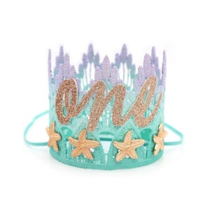 Mermaid first birthday crown with aqua lace, gold glitter starfish, and a glittery “one” topper. Perfect for a mermaid birthday party, Oneder the Sea theme, cake smash photoshoot, or beach baby shower. Handmade, lightweight, and customizable.
