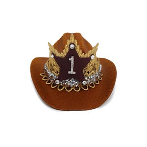 Mini brown cowboy hat made of soft felt with a gold faux leather star and metallic trim. The hat features a sparkly number one on the front for a first birthday theme. It’s lightweight, handcrafted, and designed for babies, toddlers, or small pets. Perfect for western birthday parties, rodeo photos, or dress-up costumes. Handmade in the USA by LoveCrush Crowns®.