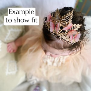 May include: Gold crown headband with pink butterfly embellishments. The crown is made of delicate lace and features a delicate floral design.