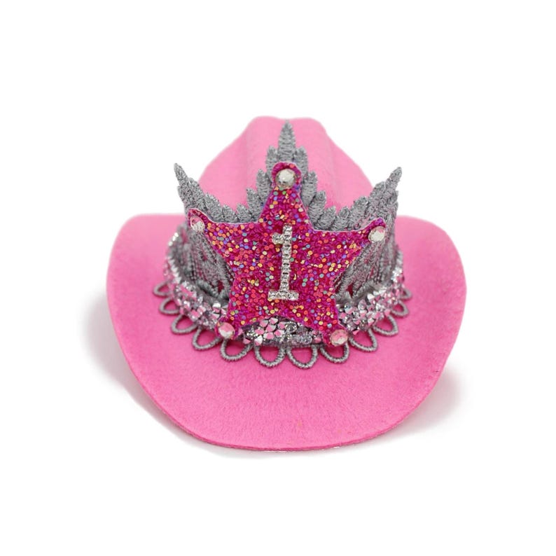 May include: A pink cowboy hat with a glittery star-shaped crown. The crown is embellished with silver accents and the number "1". The hat has a decorative silver trim around the brim, creating a festive accessory.
