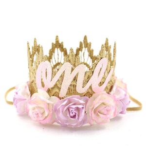 May include: Gold crown headband with pink and white fabric flowers and the word "one" in pink glitter letters.
