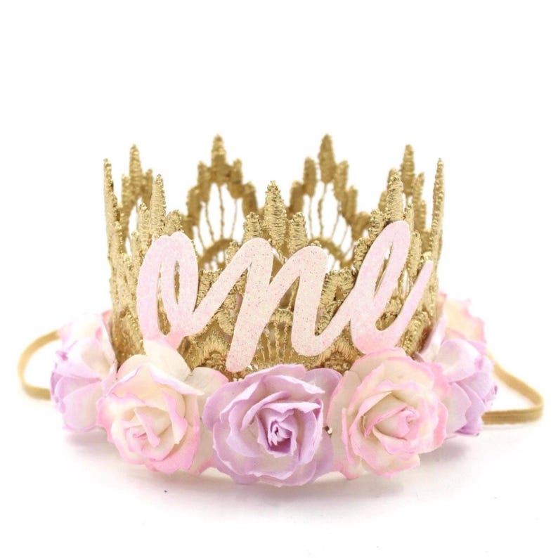 May include: Gold crown headband with pink and white fabric flowers and the word "one" in pink glitter letters.