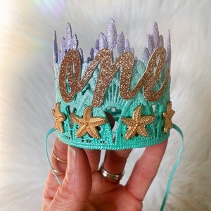 Mermaid first birthday crown with aqua lace, gold glitter starfish, and a glittery “one” topper. Perfect for a mermaid birthday party, Oneder the Sea theme, cake smash photoshoot, or beach baby shower. Handmade, lightweight, and customizable.