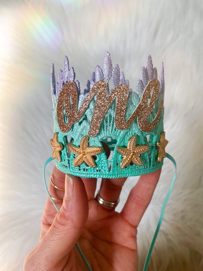 Mermaid first birthday crown with aqua lace, gold glitter starfish, and a glittery “one” topper. Perfect for a mermaid birthday party, Oneder the Sea theme, cake smash photoshoot, or beach baby shower. Handmade, lightweight, and customizable.
