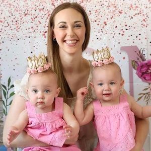 Smiling baby girl wearing a gold lace first birthday crown with pink floral accents, perfect for cake smash photos, milestone photography,  princess-themed birthday parties. A beautiful handcrafted 1st birthday tiara for an unforgettable celebration