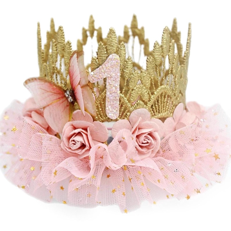 Gold lace crown with sparkly blush number 1, organza butterfly with rhinestone detail, blush pink roses, and blush pink ruffled tutu trim with gold stars. Perfect for baby girl first birthday, cake smash photoshoot, and fairy princess theme. Handmade by LoveCrush Crowns®. Can be customized in any age.