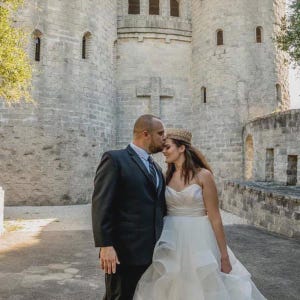Bride and groom standing close together outdoors at a castle, bride wearing a gold lace crown from LoveCrush Crowns, romantic wedding photo, elegant bridal crown styling, full lace crown for women, photoshoot inspiration