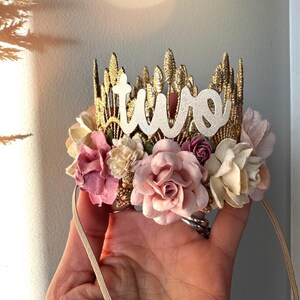 Gold lace crown with blush, and dusty pink  and white boho flowers and the word "two" in white glitter on top.  The crown is attached to a beige elastic headband.