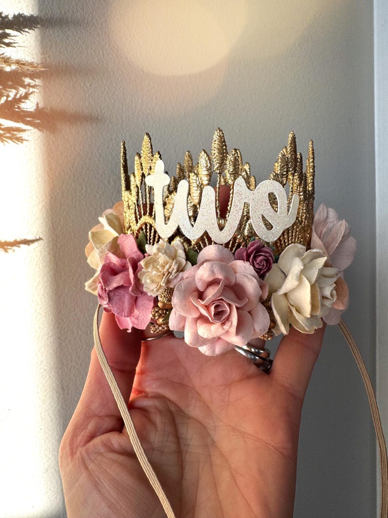 Gold lace crown with blush, and dusty pink  and white boho flowers and the word "two" in white glitter on top.  The crown is attached to a beige elastic headband.