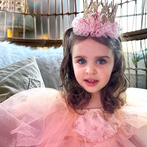 Beautiful little girl in a flowing pink tulle gown wearing a gold lace crown adorned with pink roses and a soft tutu trim. A dreamy birthday tiara for princess-themed parties, cake smash, and magical fairytale photo sessions.