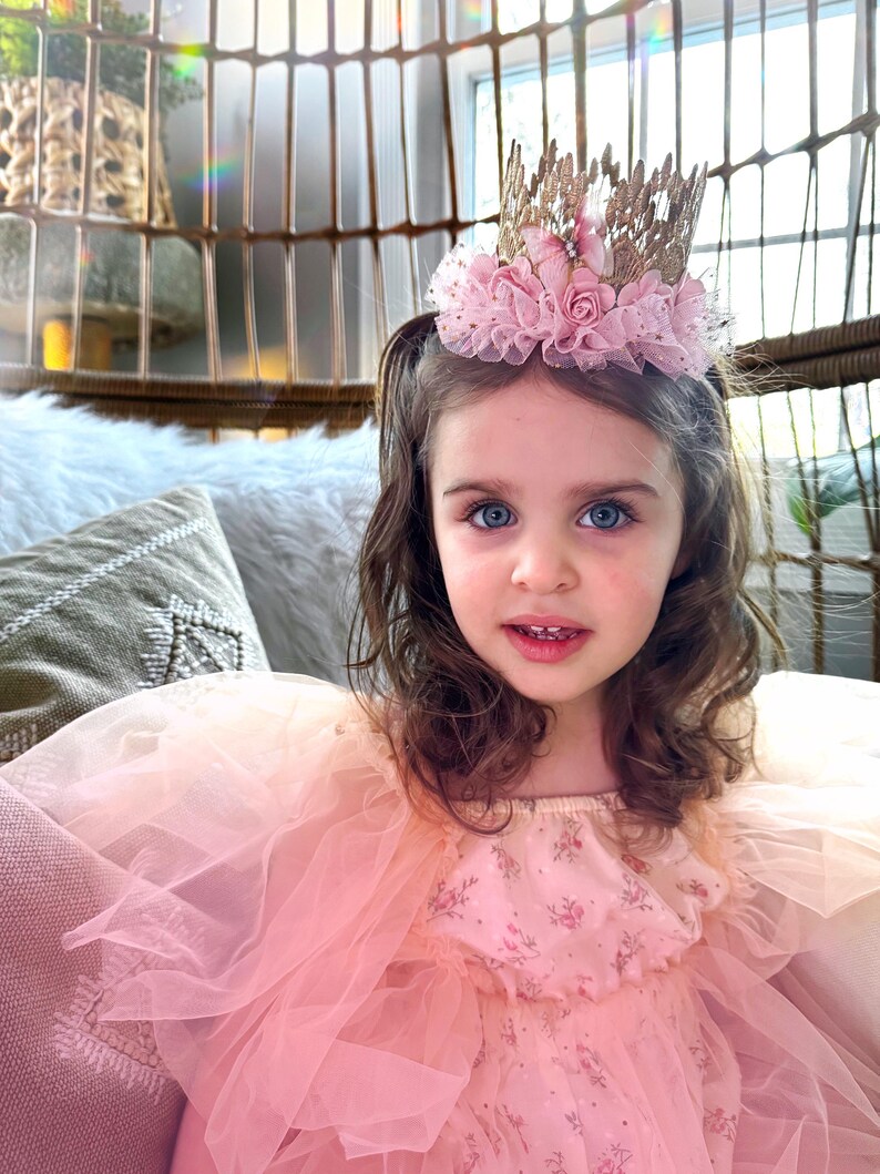 Beautiful little girl in a flowing pink tulle gown wearing a gold lace crown adorned with pink roses and a soft tutu trim. A dreamy birthday tiara for princess-themed parties, cake smash, and magical fairytale photo sessions.