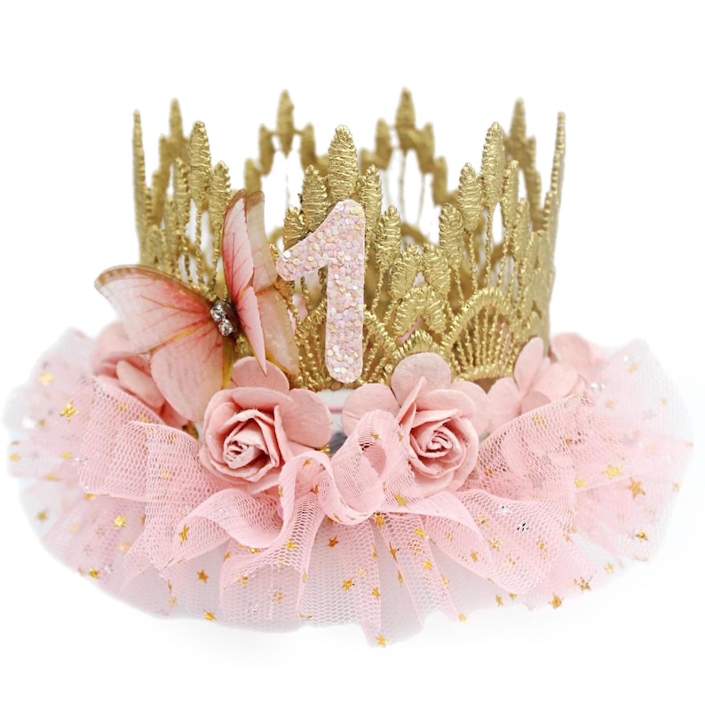Gold lace crown with sparkly blush number 1, organza butterfly with rhinestone detail, blush pink roses, and blush pink ruffled tutu trim with gold stars. Perfect for baby girl first birthday, cake smash photoshoot, and fairy princess theme. Handmade by LoveCrush Crowns®. Can be customized in any age.