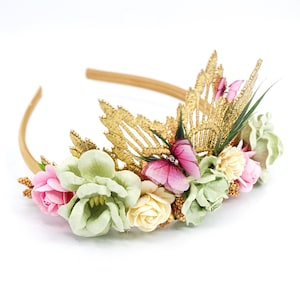 May include: A gold headband with a floral crown featuring pink and green flowers, gold leaves, and pink butterflies.