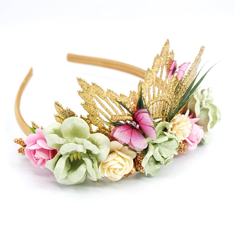 May include: A gold headband with a floral crown featuring pink and green flowers, gold leaves, and pink butterflies.