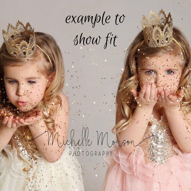 May include: Two young children wearing gold crowns and blowing glitter. One child is wearing a cream-colored dress, and the other is wearing a pink dress. The text "example to show fit" is above the children.