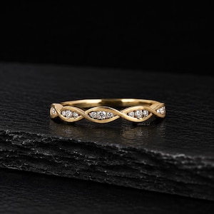 May include: A yellow gold band ring featuring a continuous twisted or infinity-style design. The metal structure forms small, open marquise-shaped settings, each containing a single round, clear, faceted gemstone embedded within the gold frame.