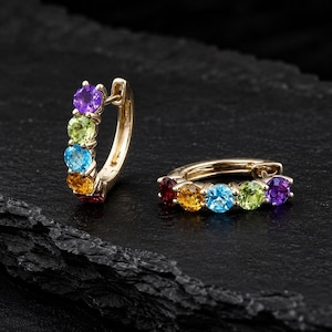Könnte beinhalten: Ein Paar Gold-Creolen mit einer Reihe von fünf rund geschliffenen, mehrfarbigen Edelsteinen in Violett, Hellgrün, Blau, Gelb und Rot. Die Ohrringe sind mit einem Klappverschluss ausgestattet, der für einen sicheren Halt sorgt.