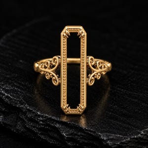 May include: A gold-toned ring featuring a tall, vertical rectangular frame with a beaded inner edge and claw-like prongs at the corners. The sides of the ring band are decorated with intricate, symmetrical scrollwork patterns.