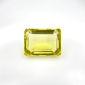 May include: A rectangular, faceted gemstone with a vibrant yellow hue. The gem has a classic emerald cut, showcasing its clarity and brilliance. The stone is set against a clean, white background, highlighting its color and shape.