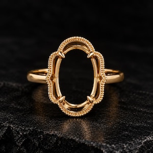 May include: A gold ring setting featuring an oval-shaped head with a beaded border and four pointed prongs. The metal has a polished finish, and the central oval opening is designed to hold a gemstone, showcasing a detailed metalwork frame.