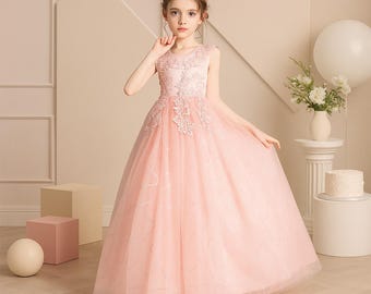 May include: A light pink sleeveless formal dress with floral embroidery on the bodice and a flowing tulle skirt. The dress is worn by a young person with a gold headband. The background includes decorative elements and a white balloon.