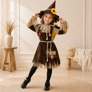 May include: A scarecrow costume featuring a brown dress with frayed hem, straw-like fringe at the sleeves and collar, and colourful patches. The outfit includes a matching pointed hat adorned with a yellow sunflower and a rope-style waist tie.