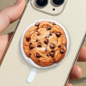 May include: A clear phone case with a chocolate chip cookie design. The case is on a beige phone with a clear border. The cookie is round with chocolate chips and a white base with a white handle.
