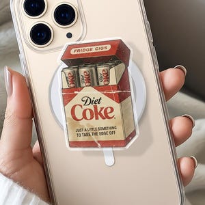May include: Clear phone case with a Diet Coke-themed design. The design features a vintage-style cigarette box labeled "Fridge Cigs" with "Diet Coke" branding and the phrase "Just a little something to take the edge off."