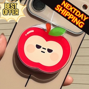 Könnte beinhalten: Ein roter, apfelförmiger Handyhalter mit einem Cartoon-Gesicht, einem grünen Blatt und einem orangefarbenen Stiel. Der Handyhalter ist an einer transparenten Handyhülle befestigt. Der Text "BEST OFFER" und "NEXTDAY SHIPPING" ist ebenfalls enthalten.