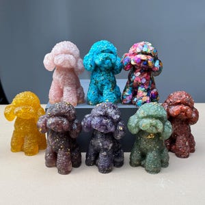 Puede incluir: Colección de nueve figuras de caniche en varios colores, incluyendo rosa, azul y amarillo. Las figuras tienen una apariencia texturizada y están dispuestas en filas. Algunas tienen motas doradas.