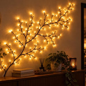 Pode incluir: Uma decoração de parede em forma de ramo iluminado com uma estrutura escura e texturizada, adornada com inúmeras pequenas luzes LED de tom quente. O ramo estende-se horizontalmente, emitindo um suave brilho dourado.