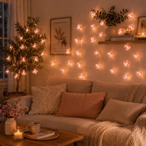 Könnte beinhalten: Eine Lichterkette mit blumenförmigen LEDs und warmweißem Licht, die an einer Wand drapiert ist und durchscheinende Blütenblätter aufweist. Die Lichter sind um einen Baum im Topf und entlang der Wand über einem beigen Sofa mit Kissen angeordnet.