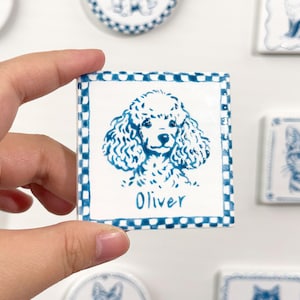 Pode incluir: Azulejo cerâmico quadrado com uma ilustração de poodle azul e o nome "Oliver". O azulejo tem uma borda quadriculada e é cercado por outros azulejos semelhantes com ilustrações de animais.