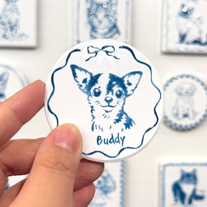 Hand holding a blue-and-white round Chihuahua portrait magnet labeled Buddy, with matching pet magnets displayed in the background.