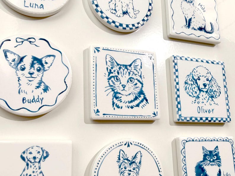 Blue-and-white ceramic pet portrait magnets displayed on a white surface, including round and square shapes with custom cat and dog illustrations.