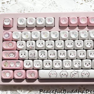 May include: A pink mechanical keyboard with custom keycaps. The keycaps are white with cute cartoon animal designs and pink accents. The keyboard has the text "Peaceful Buddha Design Keyboard Keycaps" at the bottom.