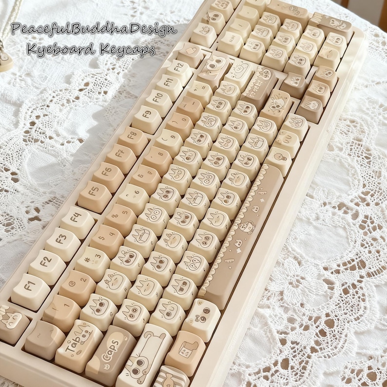 May include: A beige mechanical keyboard with custom keycaps. The keycaps feature a variety of cartoon character designs in black ink. The keyboard has a light beige frame and the text "PeacefulBuddhaDesign Keyboard Keycaps" is visible.