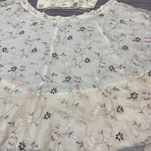 May include: Ivory-colored formal wear set featuring a crop top and a flowing skirt. The fabric is adorned with delicate floral embroidery in shades of pink, black, and silver sequins. The top has thin straps and a beaded trim.