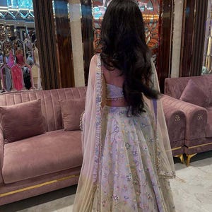 May include: A light grey lehenga with colorful floral embroidery. The outfit includes a matching top and a sheer dupatta. The text "KAMALKRITI" is visible in the bottom right corner.