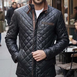 Op de afbeelding: Zwart gewatteerd leren jack met een bruine kraag en bies. De jas heeft een ruitpatroon, een ritssluiting aan de voorkant en twee voorzakken. De jas is aan de voorkant geknoopt en heeft een klassiek, stijlvol ontwerp.